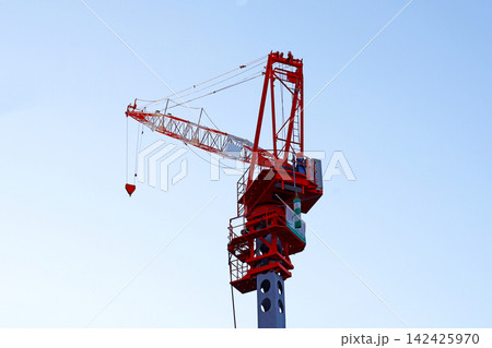 A red tower crane standing tall against a bright blue sky at a construction site. A red tower crane standing tall against a bright blue sky at a construction site. 142425970