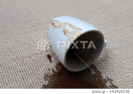 A white coffee mug creating a large brown stain on carpet. 142426236