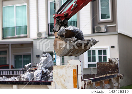 An excavator bucket scooping up broken concrete debris into a dump truck at a road construction site. An excavator bucket scooping up broken concrete debris into a dump truck at a road construction site. 142426319
