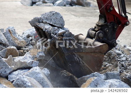 Close up of an excavator bucket digging into broken concrete blocks on a road surface. 142426502