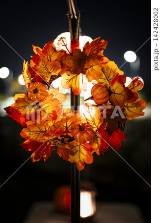 Vibrant autumn wreath with pumpkins on a pole in an outdoor night setting illustrates a cozy autumn evening spirit. 142428002