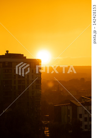 A beautiful sunset and sunny rain. Orange and amber hues of a beautiful sunset against a backdrop of fog and light rain on a summer evening. Golden hour. 142428153