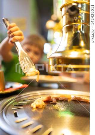 Child cooking meat on korean barbecue grill Child cooking meat on korean barbecue grill 142429011