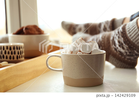 Cup of delicious hot cocoa with marshmallows near window indoors. Winter drink Cup of delicious hot cocoa with marshmallows near window indoors. Winter drink 142429109