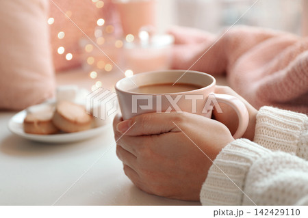 Woman holding cup of delicious hot coffee at white table, closeup. Winter drink Woman holding cup of delicious hot coffee at white table, closeup. Winter drink 142429110