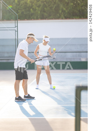 Coach teaching woman how to play tennis on a court Coach teaching woman how to play tennis on a court 142429408