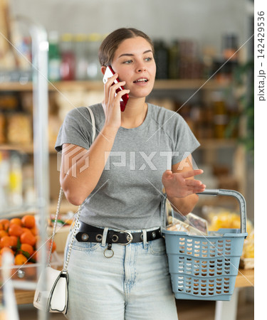 Young woman choosing groceries while talking on phone Young woman choosing groceries while talking on phone 142429536
