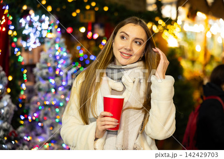 Young woman stands with glass of hot coffee in her hands and enjoys festive New Year atmosphere 142429703