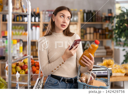 Girl customer holds bottle of peach juice in hand, scans QR code on product label Girl customer holds bottle of peach juice in hand, scans QR code on product label 142429756
