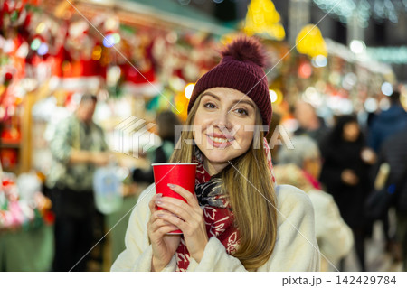 Young woman stands with glass of hot coffee in her hands and enjoys festive New Year atmosphere 142429784