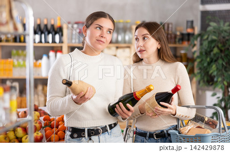 Two friends choose and buy wine together the grocery department of supermarket Two friends choose and buy wine together the grocery department of supermarket 142429878
