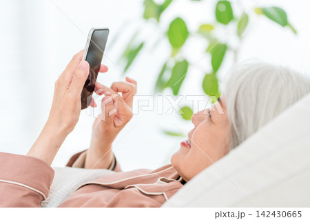 ベッドでスマートフォンを操作するグレイヘアのシニア女性 142430665