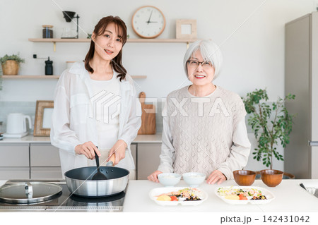 キッチンで一緒に料理を楽しむ母と娘の笑顔 キッチンで一緒に料理を楽しむ母と娘の笑顔 142431042