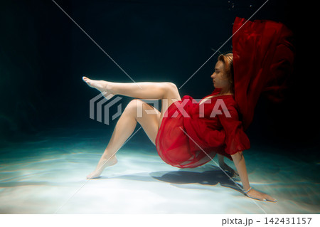 Caucasian dancer balancing in red costume in aquatic environment Caucasian dancer balancing in red costume in aquatic environment 142431157