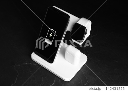 Set of gadgets charging with wireless pad on black stone table Set of gadgets charging with wireless pad on black stone table 142431223