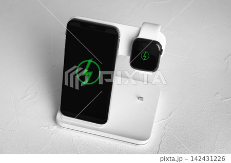 Mobile phone and smartwatch charging with wireless pad on white stone table Mobile phone and smartwatch charging with wireless pad on white stone table 142431226