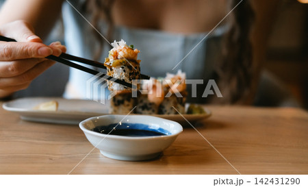 A beautiful girl eats Japanese sushi rolls with chopsticks, smiling with pleasure A beautiful girl eats Japanese sushi rolls with chopsticks, smiling with pleasure 142431290