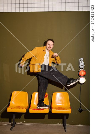Male individual standing on bright colored chairs with energetic attitude Male individual standing on bright colored chairs with energetic attitude 142431422
