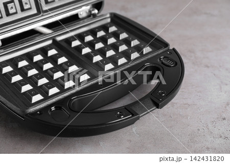 Modern waffle iron on grey stone table, closeup Modern waffle iron on grey stone table, closeup 142431820