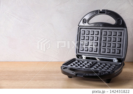 Modern waffle iron on wooden table against white background. Space for text 142431822