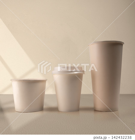 Three blank beige paper cups of different sizes lined up on a neutral surface with soft shadow overlay, perfect for packaging mockup. Mockup or Copyspace 142432238