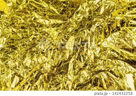 Crumpled gold foil texture background with shiny metallic wrinkles and reflective creases. Holiday, celebration or texture background 142432258
