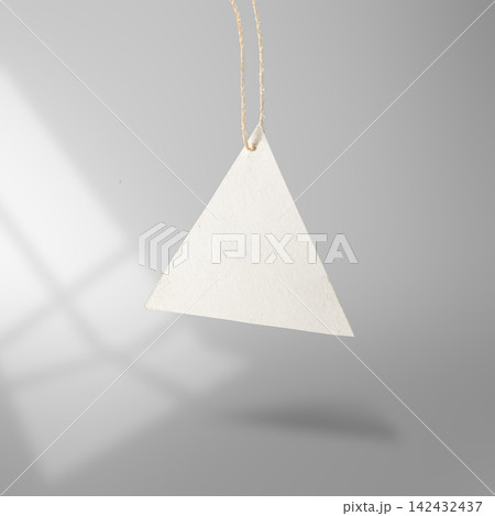 Blank triangular white paper price tag hanging from a rustic twine string against a grey background with soft shadow overlay. Mockup or Copyspace Blank triangular white paper price tag hanging from a rustic twine string against a grey background with soft shadow overlay. Mockup or Copyspace 142432437