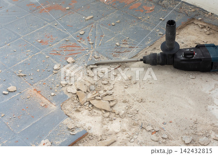 A powerful hammer drill with an orange glove rests on a concrete floor covered in debris 142432815