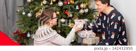 On Christmas Day, a 52-year-old couple spends time together near a decorated tree. They exchange gifts and celebrate the holiday in their cozy home setting filled with decorations On Christmas Day, a 52-year-old couple spends time together near a decorated tree. They exchange gifts and celebrate the holiday in their cozy home setting filled with decorations 142432950