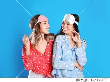 Beautiful women wearing sleeping masks on light blue background. Bedtime Beautiful women wearing sleeping masks on light blue background. Bedtime 142433102