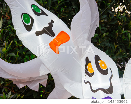 A close view of glowing inflatable ghosts highlights cheerful Halloween decorations. The illuminated display adds festive charm to an outdoor holiday setting. 142433961