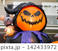 A giant inflatable Halloween reaper with a glowing pumpkin face stands outside a suburban home. The illuminated decoration adds a fun and spooky touch to the holiday display. 142433972