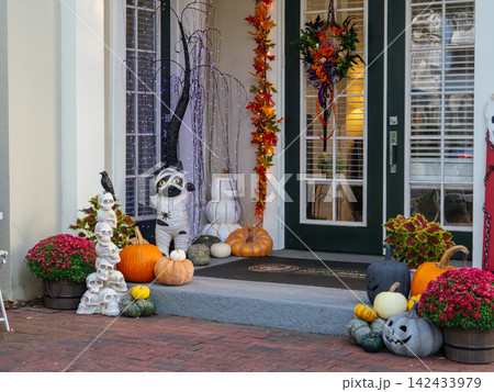 A beautifully decorated front porch features pumpkins, colorful mums, lights, and playful Halloween displays. Seasonal decorations create a warm and inviting autumn entrance. A beautifully decorated front porch features pumpkins, colorful mums, lights, and playful Halloween displays. Seasonal decorations create a warm and inviting autumn entrance. 142433979