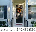 A welcoming home entrance features a colorful autumn wreath on a black front door framed by elegant white columns. Soft afternoon light creates a warm seasonal atmosphere. 142433980