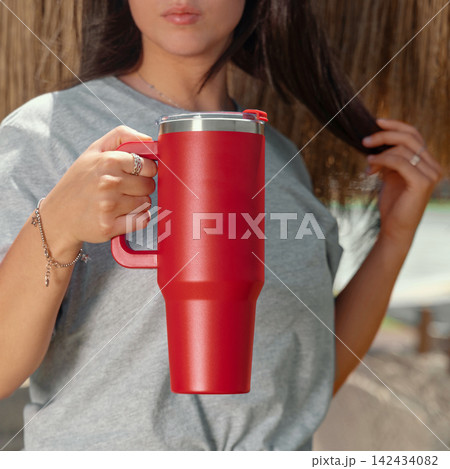 Blank red 40oz tumbler mockup, young woman outdoors, hand close up. Lifestyle scene Blank red 40oz tumbler mockup, young woman outdoors, hand close up. Lifestyle scene 142434082