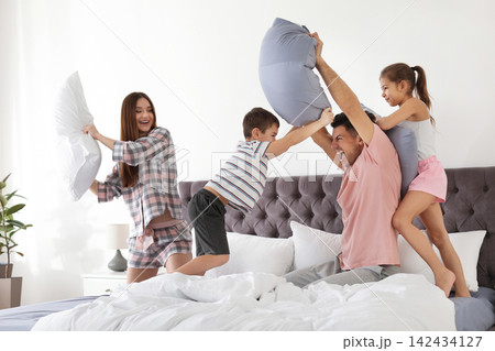 Happy family having pillow fight in bedroom 142434127