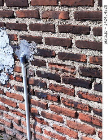A vertical white pipe on a rustic-style brick wall with cement patches. A vertical white pipe on a rustic-style brick wall with cement patches. 142434829