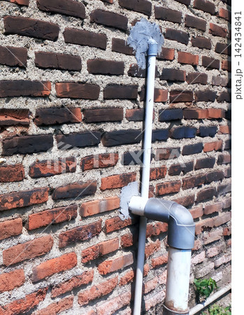 PVC pipe and elbow fitting on an exposed brick wall with cement patching. PVC pipe and elbow fitting on an exposed brick wall with cement patching. 142434841