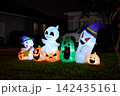 A lineup of smiling ghosts and carved pumpkin inflatables lights a suburban yard. Festive Halloween scene with vivid colors after dark. 142435161