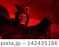 Closeup of a hooded skull figure reaching upward in deep red lighting. Halloween yard decoration with dramatic shadows against a house wall at night. 142435166