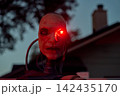 Frontal view of a cyborg head staring with a bright red eye at night. Metallic neck parts and cables create a creepy Halloween sci-fi scene. 142435170