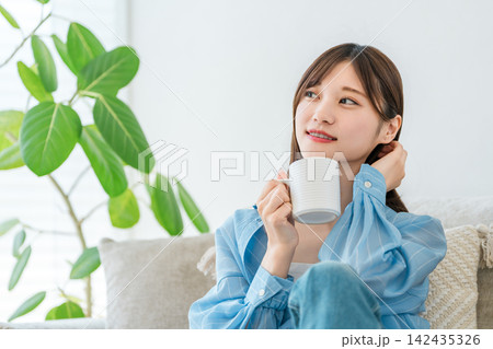 自宅のソファでコーヒー,ホットドリンクを飲みながらくつろぐ女性 142435326