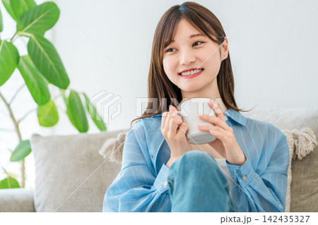 自宅のソファでコーヒー,ホットドリンクを飲みながらくつろぐ女性 自宅のソファでコーヒー,ホットドリンクを飲みながらくつろぐ女性 142435327