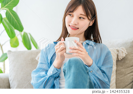 自宅のソファでコーヒー,ホットドリンクを飲みながらくつろぐ女性 142435328