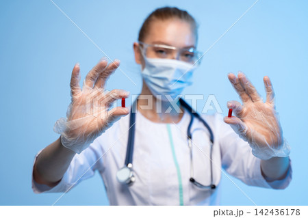 Medical professional wearing protective gear holding red capsules in gloved hands during healthcare examination 142436178