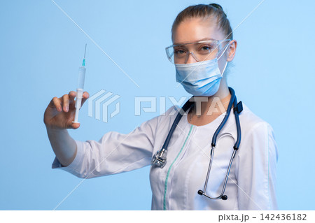 Healthcare professional wearing a protective face mask and safety glasses, holding a syringe with medicine, ready for injection Healthcare professional wearing a protective face mask and safety glasses, holding a syringe with medicine, ready for injection 142436182