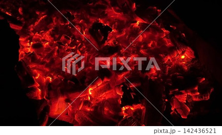Close up of glowing charcoal embers burning with red and orange tones at night. Soft heat and shimmering texture create magical atmosphere. Warm abstract scene symbolizing warmth and quiet at nature 142436521