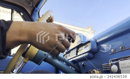 Male hands holds steering wheel while driving retro vehicle at urban street. Man riding on blue vintage auto at city road on sunny day. Driver moving in his old auto on route. Slow motion 142436539