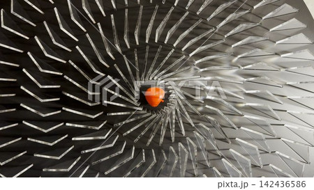 Top view on spiral geometric installation with metallic radial elements surrounding a red apple-shaped object in the center. Strong symmetry, depth and optical movement create a striking visual focus Top view on spiral geometric installation with metallic radial elements surrounding a red apple-shaped object in the center. Strong symmetry, depth and optical movement create a striking visual focus 142436586