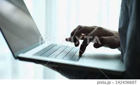 Male hand of young businessman typing text on laptop keyboard near window in modern office. Professional manager working on computer with natural light, showing productivity and communication Male hand of young businessman typing text on laptop keyboard near window in modern office. Professional manager working on computer with natural light, showing productivity and communication 142436607